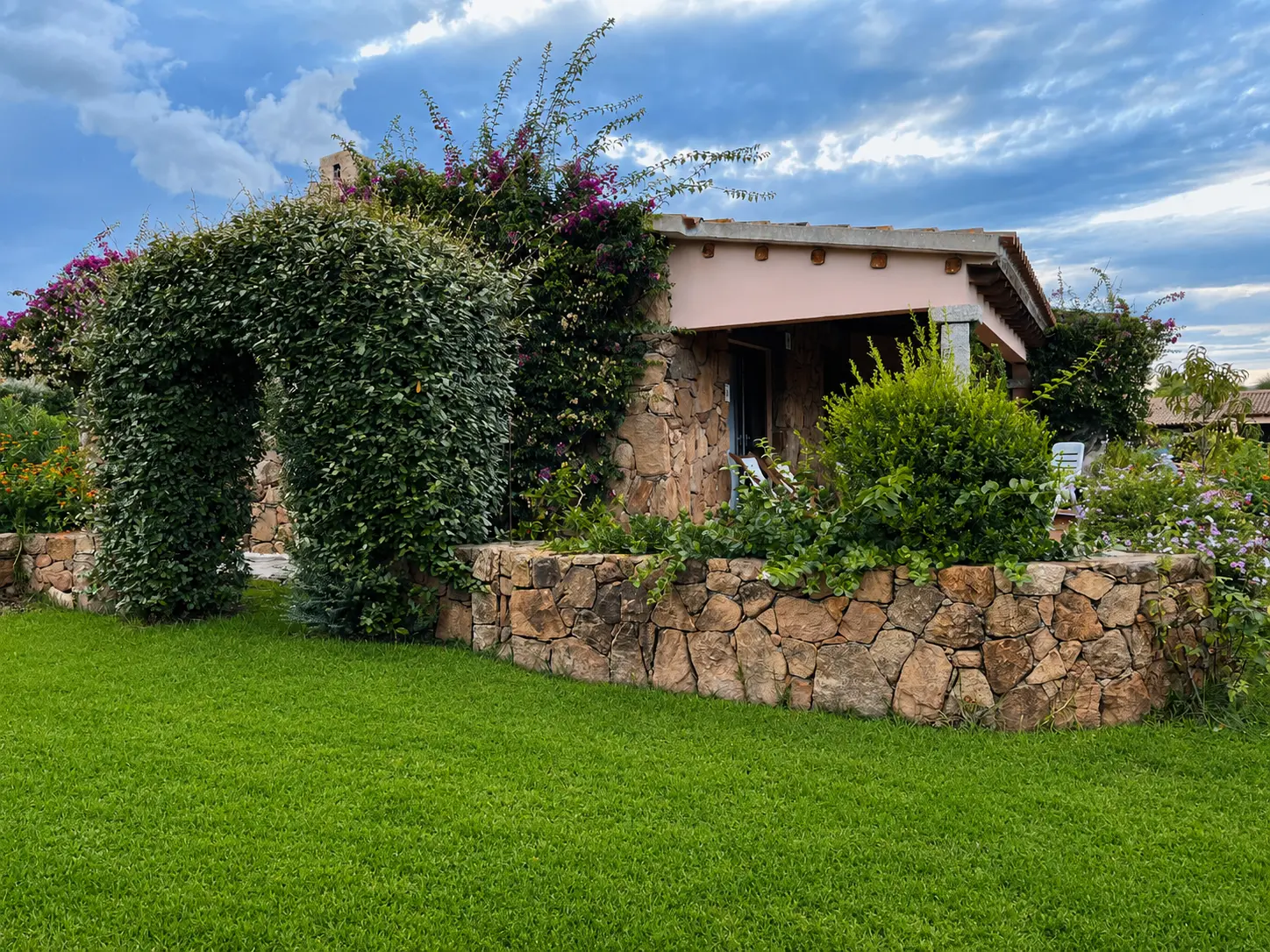 Stone villa exterior with flowering jasmine arch and private lawn