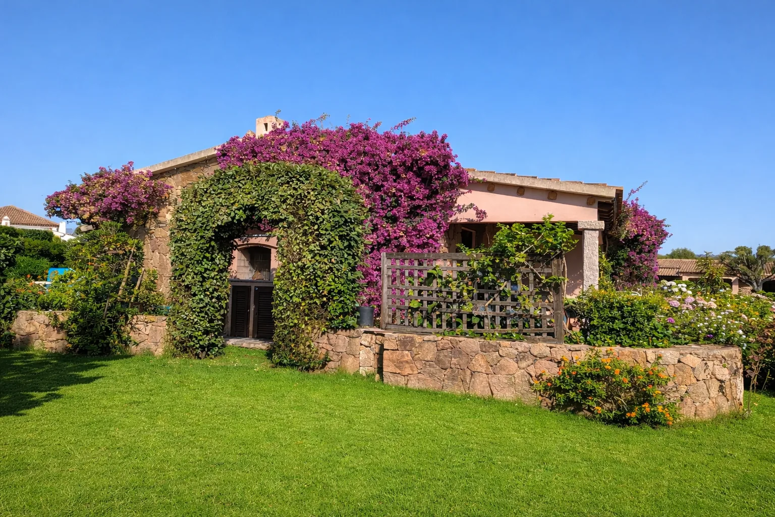San Teodoro Beach Villa 86B, a stone house near the beach, covered in bougainvillea above its private lawn