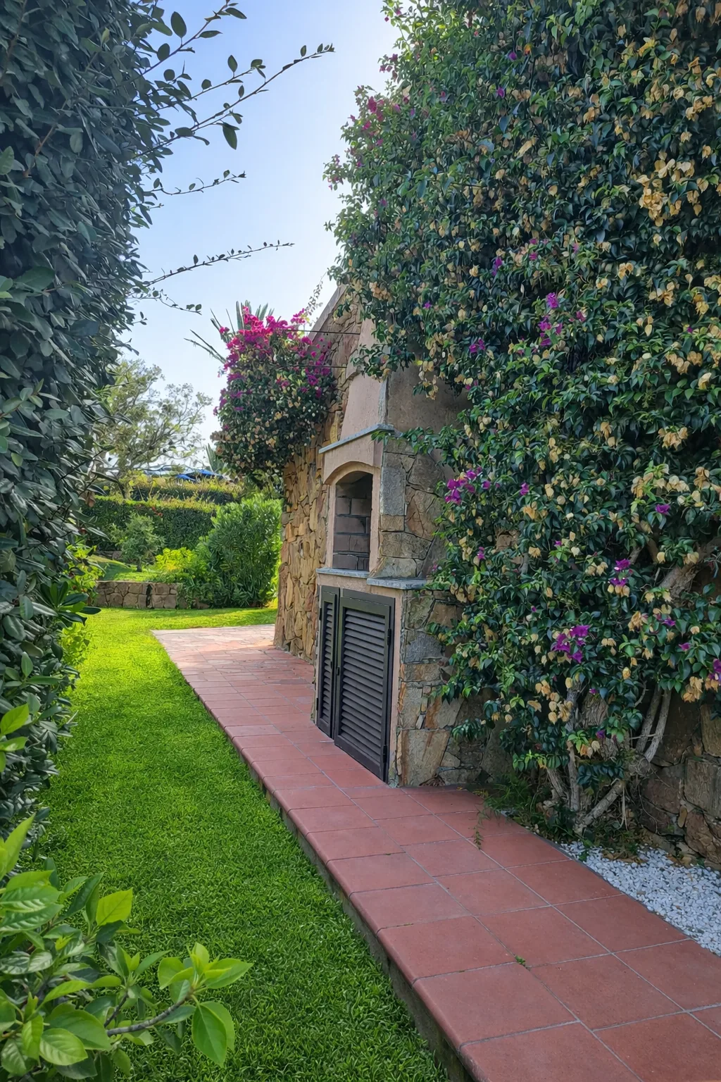 Tiled garden path past the stone barbecue and bougainvillea toward the lawn