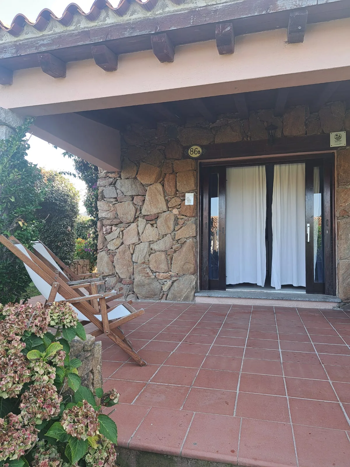 Front patio with deckchairs by the stone wall and the sliding doors of villa 86B