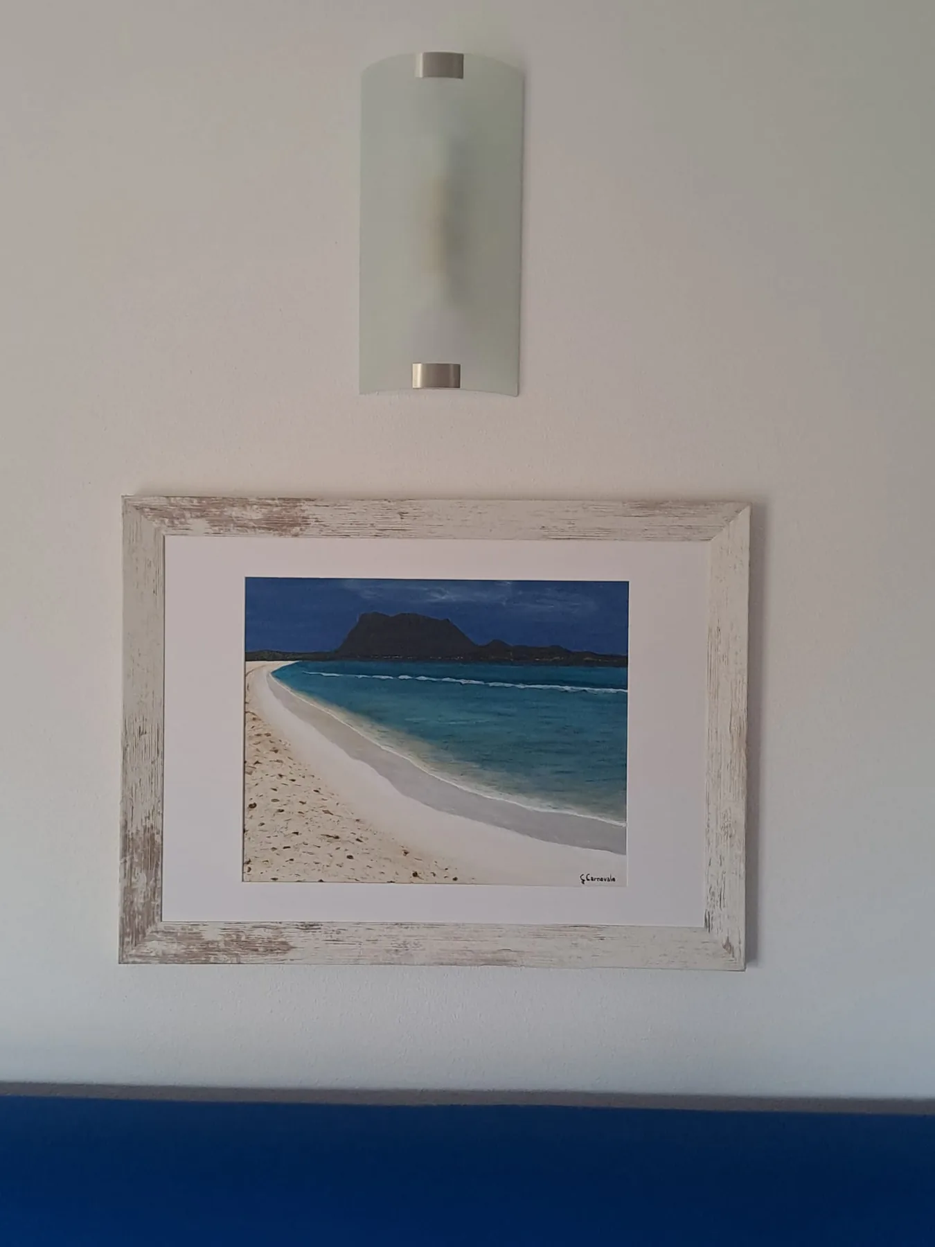 Painting of a white beach and Tavolara island hanging above the blue sofa