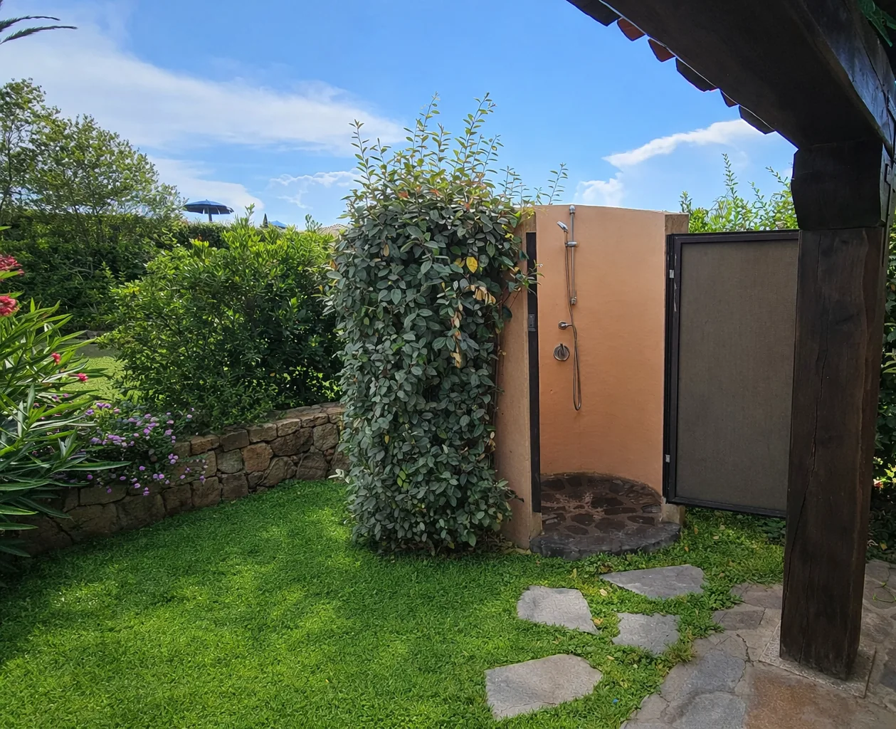 Outdoor shower with its door open, set in the garden beside the pergola